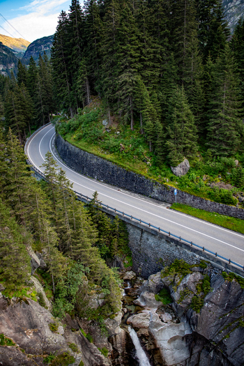 Aerial view of a winding road crossing a stone bridge over a waterfall in the Swiss Alps near Airolo Ticino Switzerland. Aerial view of a winding road crossing a stone bridge over a waterfall in the Swiss Alps near Airolo Ticino Switzerland.