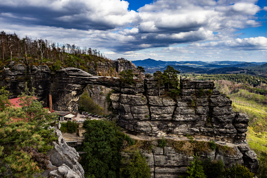 View of Pravcicka brana a natural sandstone arch formation surrounded by forest and rugged rock formations under a cloudy sky Hrensko Usti nad Labem Region Czechia.