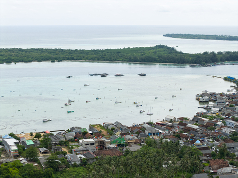 Aerial view of the turquoise waters speckled with boats contrast against the dense green islands and the vibrant village hugging the coastline Karimunjawa Central Java Indonesia. Aerial view of the turquoise waters speckled with boats contrast against the dense green islands and the vibrant village hugging the coastline Karimunjawa Central Java Indonesia.