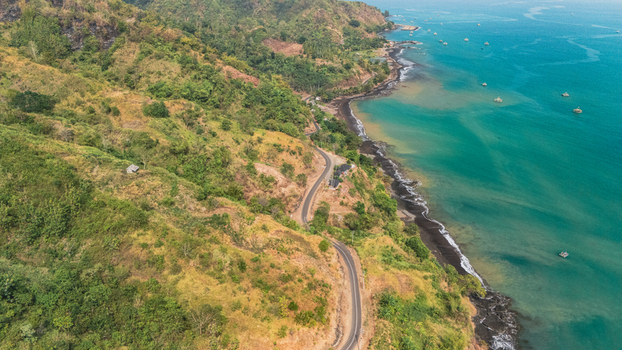 Aerial view of a winding coastal road along lush green hills and the turquoise sea in Sukabumi Indonesia. Aerial view of a winding coastal road along lush green hills and the turquoise sea in Sukabumi Indonesia.