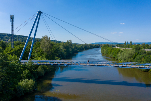 Aerial view of Lila Brucke pedestrian bridge crossing the Regnitz river with lush green trees and a person on the walkway Forchheim Bavaria Germany. Aerial view of Lila Brucke pedestrian bridge crossing the Regnitz river with lush green trees and a person on the walkway Forchheim Bavaria Germany.
