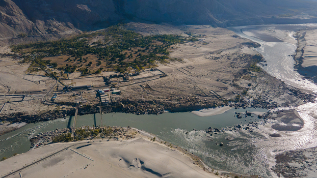 Aerial view of the Indus River flowing through the rugged landscape with sandy banks and a bridge crossing near Skardu Gilgit Pakistan.