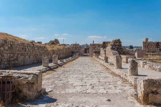 View of the historic Umayyad Palace ruins featuring ancient stone walls a paved walkway and crumbling columns under a clear blue sky in Amman Amman Governorate Jordan.
