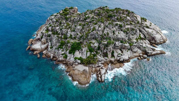 Aerial view of a rocky islet surrounded by turquoise ocean water off the coast of Grand Anse Village Grand Anse Mahe Seychelles. Aerial view of a rocky islet surrounded by turquoise ocean water off the coast of Grand Anse Village Grand Anse Mahe Seychelles.
