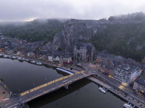 Aerial view of the Collegiate Church of Notre Dame de Dinant along the Meuse River with a bridge historic buildings and dramatic cliffs in the background in Dinant Wallonia Belgium. Aerial view of the Collegiate Church of Notre Dame de Dinant along the Meuse River with a bridge historic buildings and dramatic cliffs in the background in Dinant Wallonia Belgium.