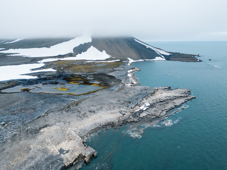 Svalbard and Jan Mayen 28 July 2025 Aerial view of the rugged arctic coastline with snow patches rocky shores and a fog shrouded mountain peak under an overcast sky. Svalbard and Jan Mayen 28 July 2025 Aerial view of the rugged arctic coastline with snow patches rocky shores and a fog shrouded mountain peak under an overcast sky.