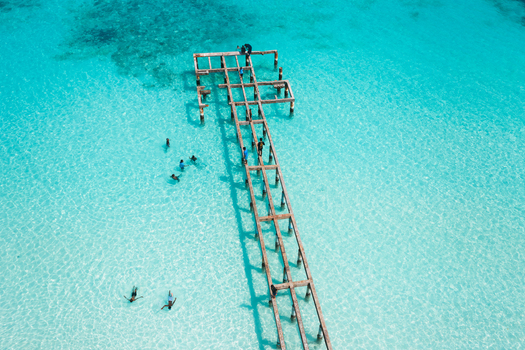 Aerial view of a weathered wooden jetty extending into crystal clear turquoise waters with people swimming and walking on the structure in Vashafaru Haa Alif Atoll Maldives. Aerial view of a weathered wooden jetty extending into crystal clear turquoise waters with people swimming and walking on the structure in Vashafaru Haa Alif Atoll Maldives.