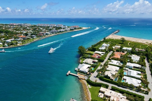 Aerial view of Palm Beach Inlet with luxury waterfront estates boats cruising through turquoise waters and the Atlantic Ocean horizon under a clear sky Palm Beach Florida United States. Aerial view of Palm Beach Inlet with luxury waterfront estates boats cruising through turquoise waters and the Atlantic Ocean horizon under a clear sky Palm Beach Florida United States.