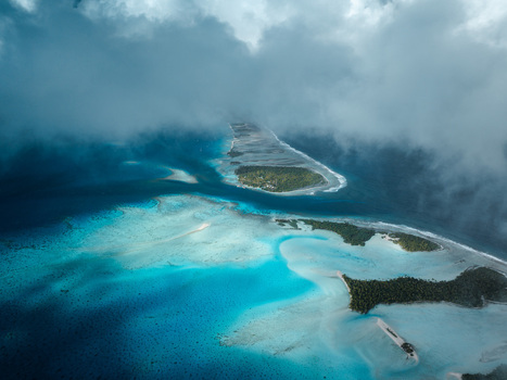 Aerial view of tropical atolls and turquoise lagoons surrounded by coral reefs under dramatic clouds in Moorea Maiao Windward Islands French Polynesia. Aerial view of tropical atolls and turquoise lagoons surrounded by coral reefs under dramatic clouds in Moorea Maiao Windward Islands French Polynesia.