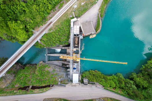 Aerial view of the Lac du Vernex dam with a yellow construction crane turquoise water and a railway bridge surrounded by green forest Rossiniere Vaud Switzerland.