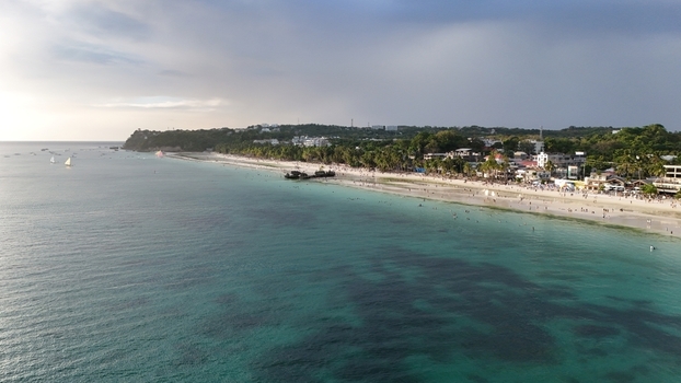 Malay Philippines 02 May 2026 Aerial view of Boracay Island featuring turquoise waters white sand beach people swimming and coastal resorts under a cloudy sky.