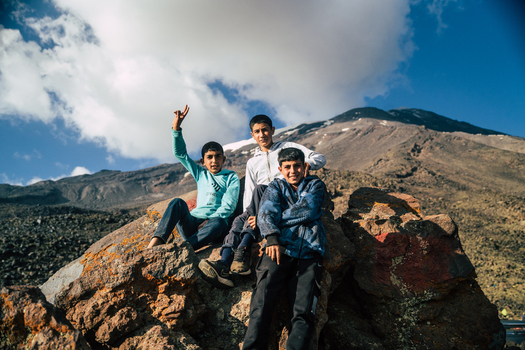 Turkey 14 August 2023 View of three young boys sitting on a large rock with the volcanic slopes of Mount Ararat in the background under a clear blue sky. Turkey 14 August 2023 View of three young boys sitting on a large rock with the volcanic slopes of Mount Ararat in the background under a clear blue sky.