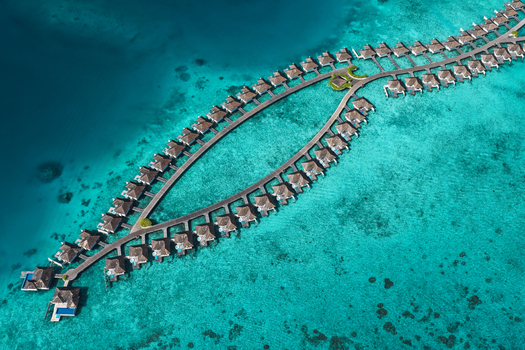 Aerial view of overwater bungalows arranged in a curved walkway over the turquoise lagoon of the Indian Ocean in Kudahuvadhoo Dhaalu Atoll Maldives. Aerial view of overwater bungalows arranged in a curved walkway over the turquoise lagoon of the Indian Ocean in Kudahuvadhoo Dhaalu Atoll Maldives.