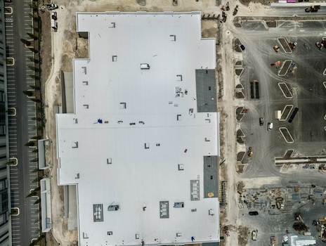 Aerial view of a large commercial building under construction on Foundry Lane with a white flat roof and surrounding parking lot layout in World Golf Village Florida United States.