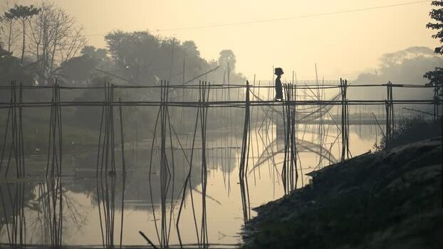 View of a person crossing a bamboo bridge at sunrise Bangladesh. View of a person crossing a bamboo bridge at sunrise Bangladesh.