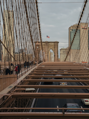 View of the Brooklyn Bridge with traffic on the roadway pedestrians walking on the side and skyscrapers in the background in New York New York United States.