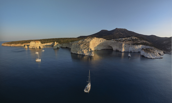 Aerial view of the dramatic white volcanic cliffs and turquoise waters of Kleftiko cove with sailboats anchored in the bay in Milos Greece. Aerial view of the dramatic white volcanic cliffs and turquoise waters of Kleftiko cove with sailboats anchored in the bay in Milos Greece.