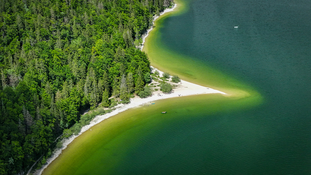 Aerial view of the lush forest meets the serene waters of Lac de Joux where the interplay of light paints the sandy shores with hues of emerald Le Lieu Vaud Switzerland.