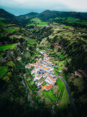 Aerial view of a vibrant village nestled amidst rolling green hills and winding roads contrasting with the cloudy sky Agua de Alto Azores Portugal.