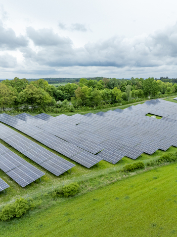 Aerial view of a large solar panel farm installed in a lush green field surrounded by dense forest under a cloudy sky Aiglsbach Bavaria Germany.