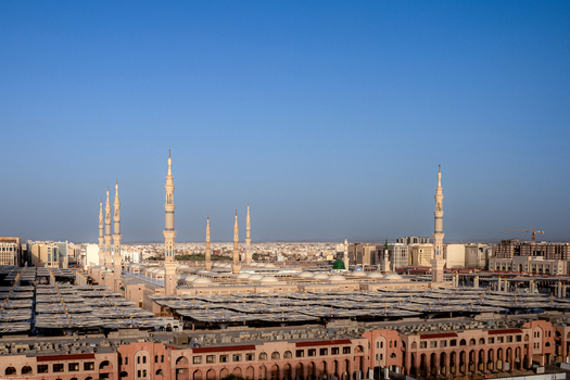 View of Al Masjid e Nabawi with its iconic minarets and expansive courtyards under a clear blue sky in Madinah Al Madinah Province Saudi Arabia.