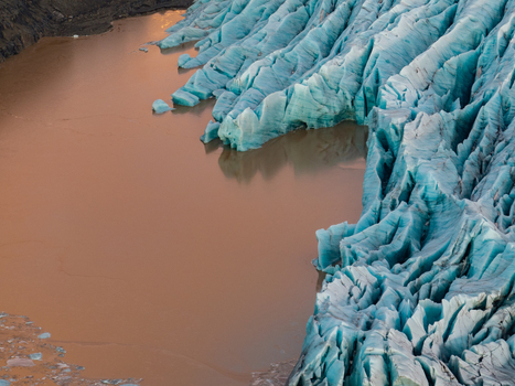 Aerial view of Svinafellsjokull glacier with its deep blue crevasses and ice formations meeting a glacial lagoon with sediment rich water Sveitarfelagid Hornafjordur Iceland. Aerial view of Svinafellsjokull glacier with its deep blue crevasses and ice formations meeting a glacial lagoon with sediment rich water Sveitarfelagid Hornafjordur Iceland.