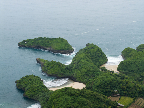 Aerial view of lush green islands rugged cliffs golden sands and white waves meeting the sea Gunungkidul Regency Special Region of Yogyakarta Indonesia. Aerial view of lush green islands rugged cliffs golden sands and white waves meeting the sea Gunungkidul Regency Special Region of Yogyakarta Indonesia.