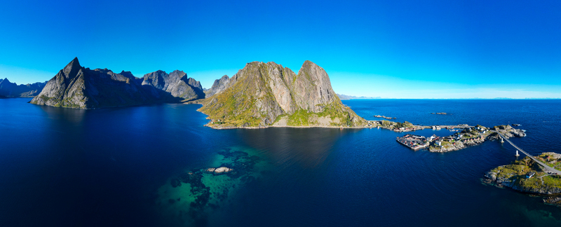 Aerial view of Hamnoy village with its iconic red cabins rugged mountain peaks and deep blue sea under a clear sky in the Lofoten archipelago Hamnoy Nordland Norway. Aerial view of Hamnoy village with its iconic red cabins rugged mountain peaks and deep blue sea under a clear sky in the Lofoten archipelago Hamnoy Nordland Norway.