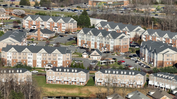 Aerial view of a modern residential apartment complex with multi story buildings parking lots paved roads and landscaped green spaces in Forest Virginia United States.