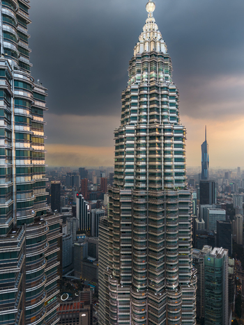 Kuala Lumpur Malaysia 11 March 2026 Aerial view of the Petronas Twin Towers rising above the city skyline under a dramatic sunset sky with dark clouds.
