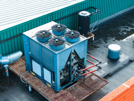 Aerial view of a large blue industrial HVAC chiller unit situated on a rooftop with metal grating pipes and a green corrugated wall in Riga Latvia. Aerial view of a large blue industrial HVAC chiller unit situated on a rooftop with metal grating pipes and a green corrugated wall in Riga Latvia.