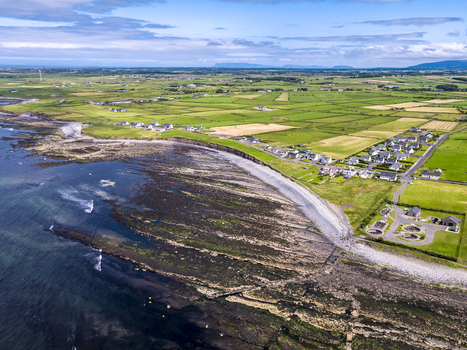 Aerial view of Storm Beach with its rocky shoreline adjacent green agricultural fields and a small residential village in Carrownedin County Sligo Ireland.