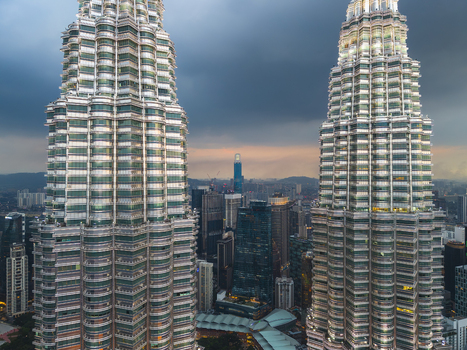 Kuala Lumpur Malaysia 11 March 2026 Aerial view of the Petronas Twin Towers rising above the city skyline under a dramatic sunset sky with dark clouds.