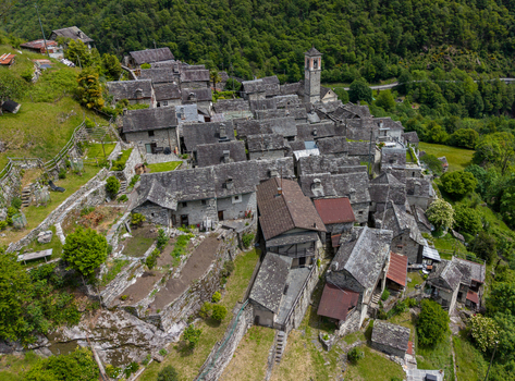 Aerial view of the historic Corippo Albergo Diffuso village with traditional stone houses and a church tower nestled on a lush green hillside in Corippo Ticino Switzerland. Aerial view of the historic Corippo Albergo Diffuso village with traditional stone houses and a church tower nestled on a lush green hillside in Corippo Ticino Switzerland.