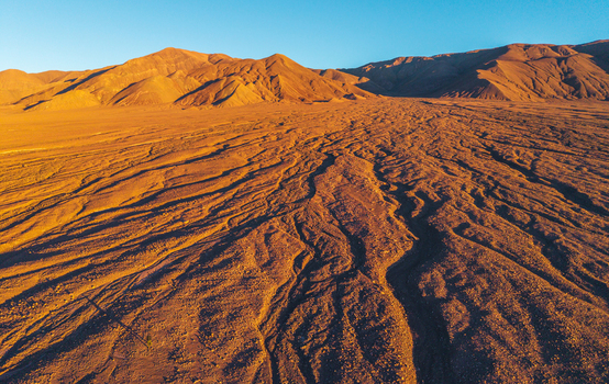 Aerial view of the arid desert landscape with intricate erosion patterns and golden light on the sand dunes in San Pedro de Atacama Antofagasta Chile. Aerial view of the arid desert landscape with intricate erosion patterns and golden light on the sand dunes in San Pedro de Atacama Antofagasta Chile.