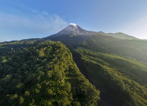 Aerial view of Mount Merapi volcano with smoke rising from its crater above the lush green forests of the Kaliadem area in Kecamatan Pakem Daerah Istimewa Yogya Indonesia. Aerial view of Mount Merapi volcano with smoke rising from its crater above the lush green forests of the Kaliadem area in Kecamatan Pakem Daerah Istimewa Yogya Indonesia.