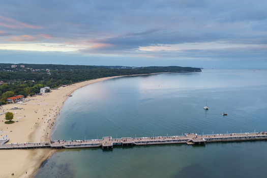 Aerial view of the Sopot Pier extending into the Baltic Sea with a sandy beach lush coastal forest and people walking along the wooden structure in Sopot Pomeranian Voivodeship Poland. Aerial view of the Sopot Pier extending into the Baltic Sea with a sandy beach lush coastal forest and people walking along the wooden structure in Sopot Pomeranian Voivodeship Poland.