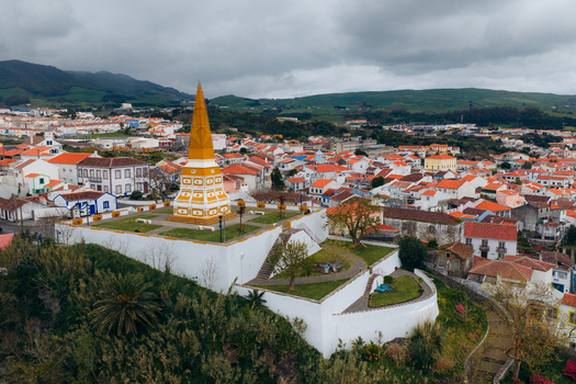 Aerial view of Alto da Memoria monument overlooking the historic city center with red tiled roofs and green hills under a cloudy sky Angra do Heroismo Azores Portugal.