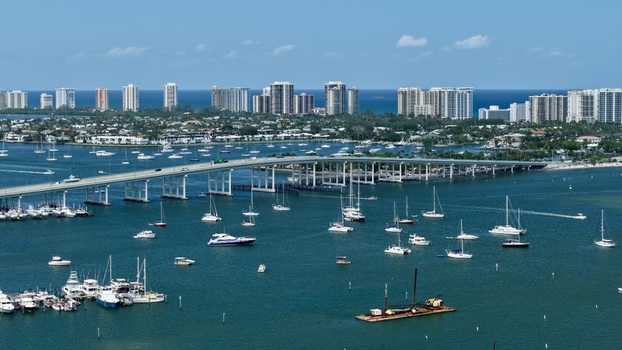 Aerial view of Peanut Island and the Blue Heron Bridge with numerous boats anchored in the turquoise water and the coastal skyline Palm Beach County Florida United States.