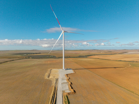 Aerial view of a single wind turbine with red tipped blades standing in a vast agricultural field under a clear blue sky in Swellendam Western Cape South Africa. Aerial view of a single wind turbine with red tipped blades standing in a vast agricultural field under a clear blue sky in Swellendam Western Cape South Africa.