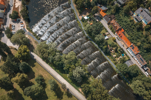 Aerial view of a stepped river weir surrounded by lush trees and urban buildings in Saalfeld Thuringia Germany. Aerial view of a stepped river weir surrounded by lush trees and urban buildings in Saalfeld Thuringia Germany.