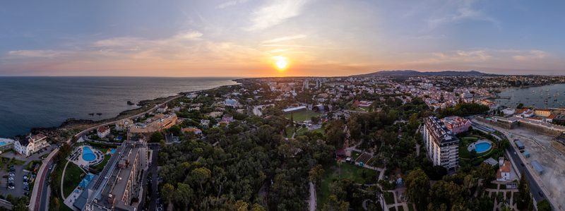 Aerial view of the coastal town of Cascais at sunset featuring the Atlantic Ocean lush greenery and residential architecture in Cascais Lisboa Portugal. Aerial view of the coastal town of Cascais at sunset featuring the Atlantic Ocean lush greenery and residential architecture in Cascais Lisboa Portugal.