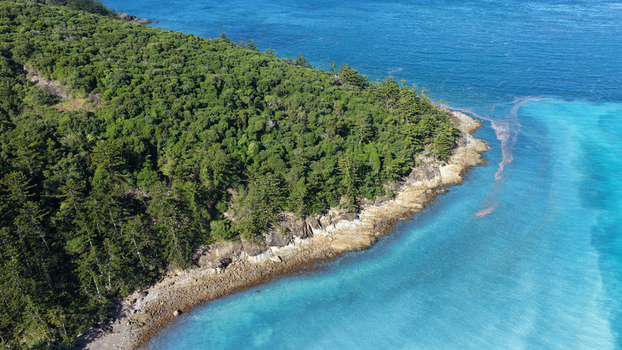 Aerial view of Chance Bay featuring lush green coastal forest meeting turquoise waters and rocky shoreline in Whitsundays Queensland Australia. Aerial view of Chance Bay featuring lush green coastal forest meeting turquoise waters and rocky shoreline in Whitsundays Queensland Australia.