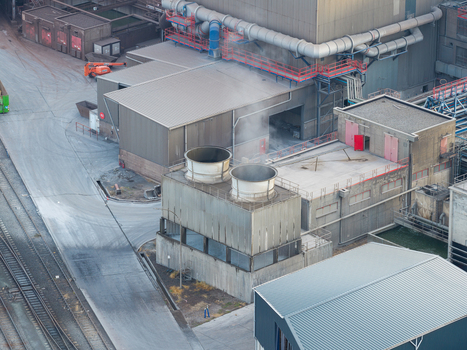 Aerial view of the Haven Genk industrial facility featuring large cooling towers emitting steam surrounded by steel plant infrastructure and railway tracks in Genk Vlaanderen Belgium.