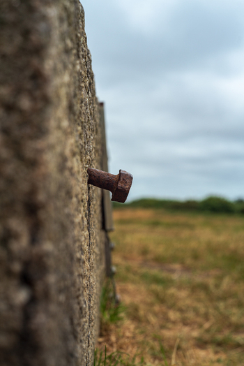View of a rusty metal bolt protruding from a weathered concrete wall in a field in Bodmin Cornwall United Kingdom. View of a rusty metal bolt protruding from a weathered concrete wall in a field in Bodmin Cornwall United Kingdom.