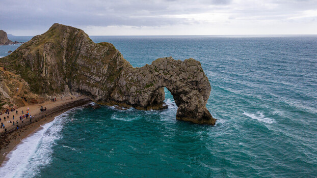 Aerial view of Durdle Door a natural limestone arch with turquoise sea rocky cliffs and people on the beach in Wareham England United Kingdom. Aerial view of Durdle Door a natural limestone arch with turquoise sea rocky cliffs and people on the beach in Wareham England United Kingdom.
