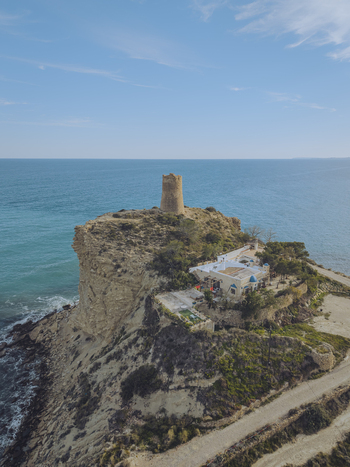 Aerial view of Torre del Xarco a historic watchtower perched on a rugged cliff overlooking the turquoise Mediterranean Sea and coastal vegetation La Vila Joiosa Comunidad Valenciana Spain.
