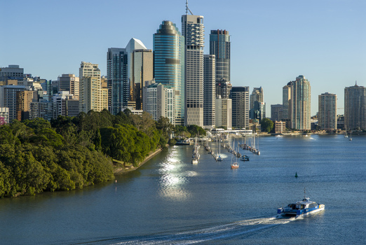 View of the Brisbane city skyline with modern skyscrapers the Brisbane River a ferry boat cruising on the water and lush parkland in Brisbane Queensland Australia.
