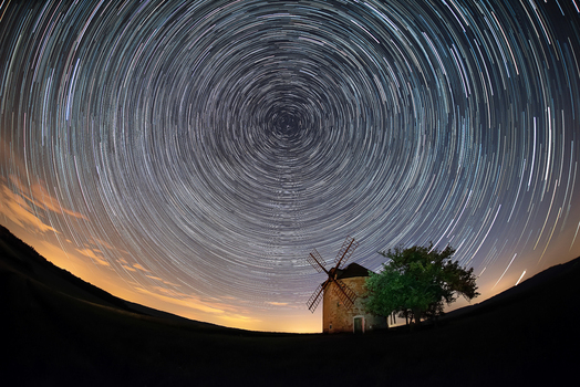 View of a historic windmill under a night sky filled with circular star trails in a rural landscape in Brno City District South Moravian Region Czechia.