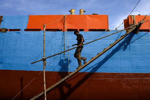 Keraniganj Bangladesh 31 August 2024 View of a worker walking down a wooden ladder from a large ship painted in bright blue and orange at the Shipyard Dhaka.